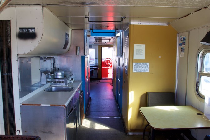 Interior of caboose, with counter and sink on right and table with chair on left.