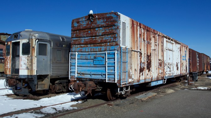Freight cars and passenger cars with rusting and fading paint.