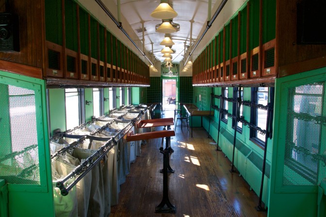 Interior of postal car, with sacks hanging in bins on the left, lockers above in the luggage rack, and post office boxes in the background.