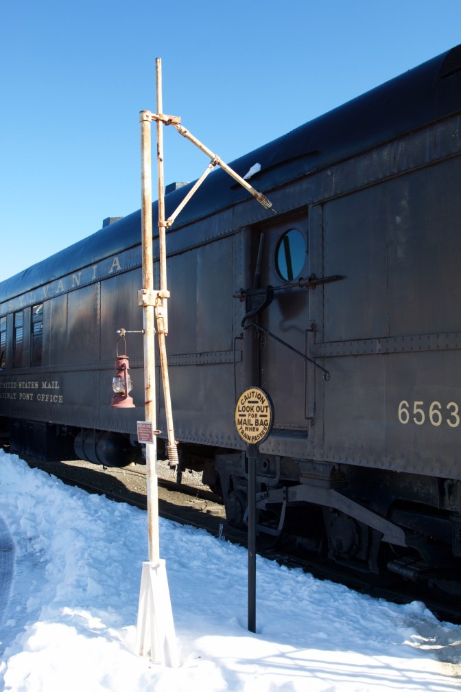 Pole and hook next to postal car, with sign CAUTION LOOK OUT FOR MAIL BAG WHEN TRAIN PASSES.