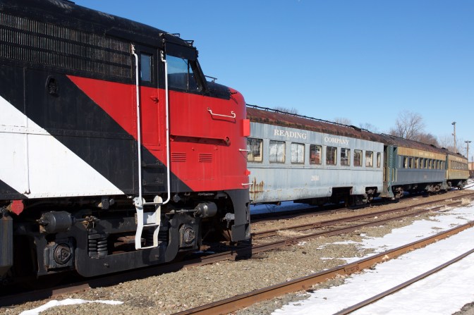 Red engine on one track, with passenger cars on the track beside it.