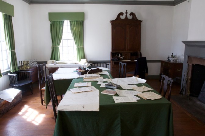 Field office of George Washington, with maps and orders on the tables. A fireplace is on the right of the image. And two windows are on the left.