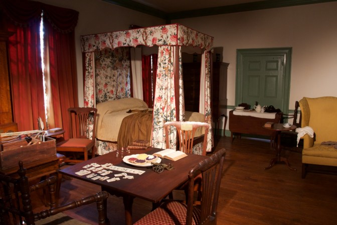 Interior of first-floor bedroom, with a table with card games, a four-poster bed, a desk, and two chairs.