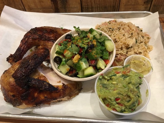 Half chicken, rice, cucumber salad, and guacamole, on a metal tray with a paper liner.