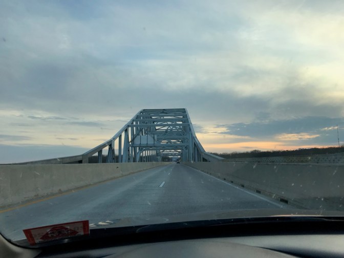 View of bridge through car windshield, with clouds in the distance.