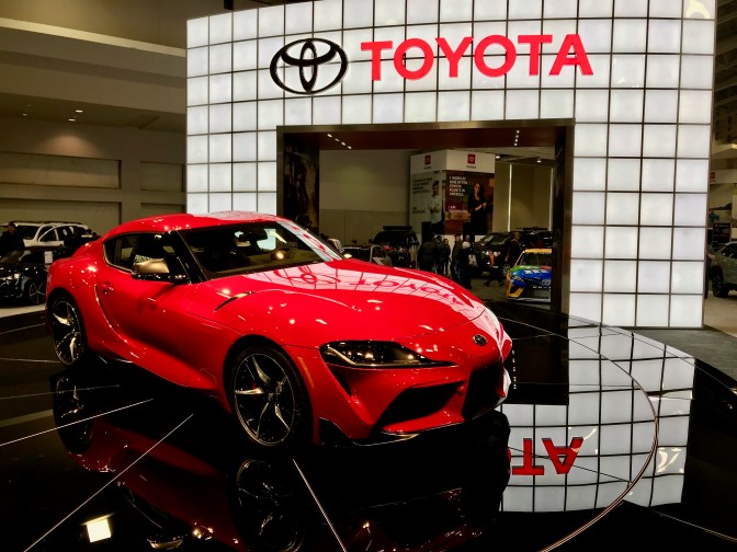 Red Toyota Supra on black pedestal, with Red Toyota sign in the background.