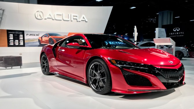 Red Acura NSX, with large Acura sign in the background.
