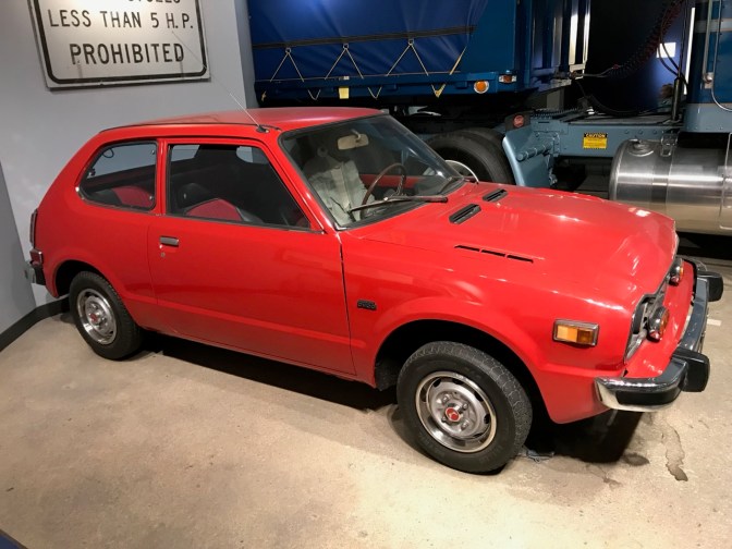 Red 1977 Honda Civic hatchback. A semi is in the background.