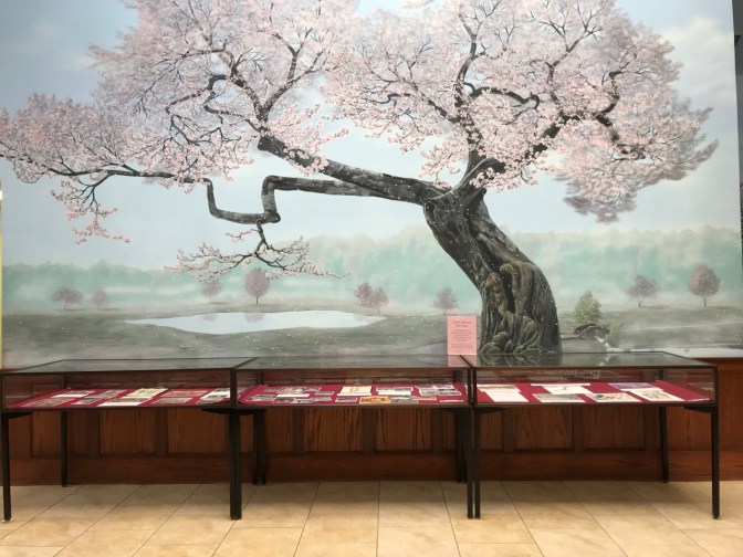 Mural of tree in front of glass display cases with information on cherry blossom trees.