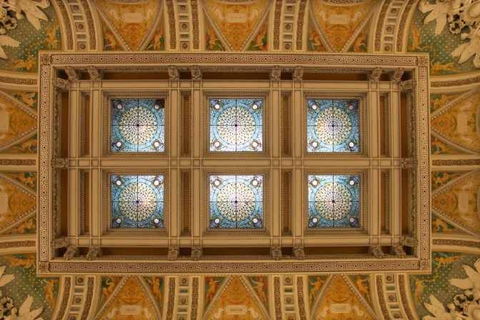 Ceiling of the Great Hall, with stained glass skylights surrounded by an elaborately decorated ceiling.