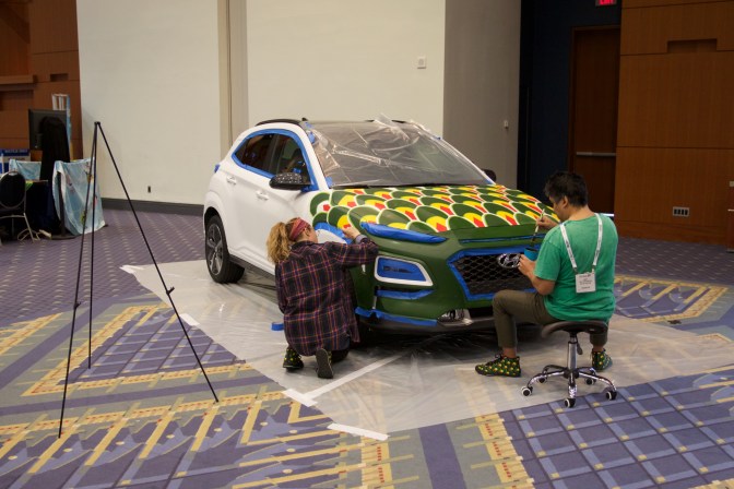 Two artists painting a Hyundai hatchback.