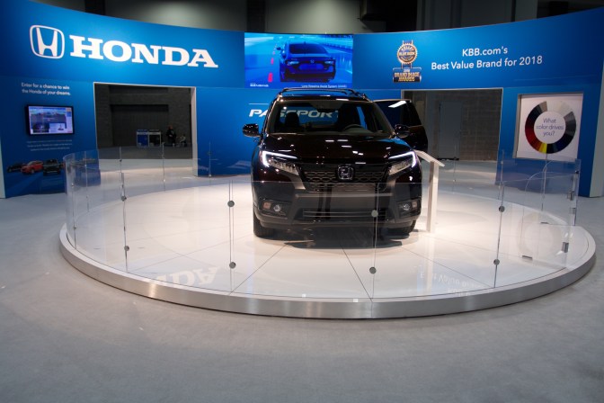 2019 Honda Passport SUV in black, on a circular pedestal in front of a Honda marquee.
