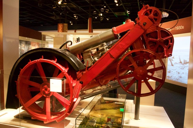 Tractor, with red and gold framework, standing on its rear wheels.