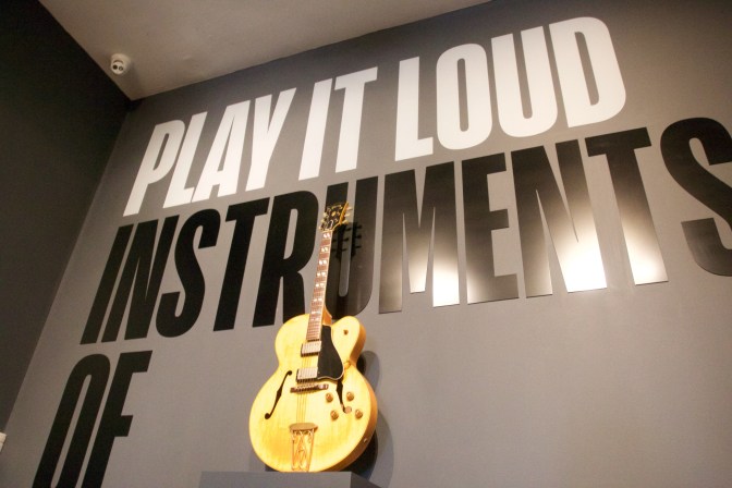 Gibson Hollow-body electric guitar in front of wall sign that says PLAY IT LOUD INSTRUMENTS OF