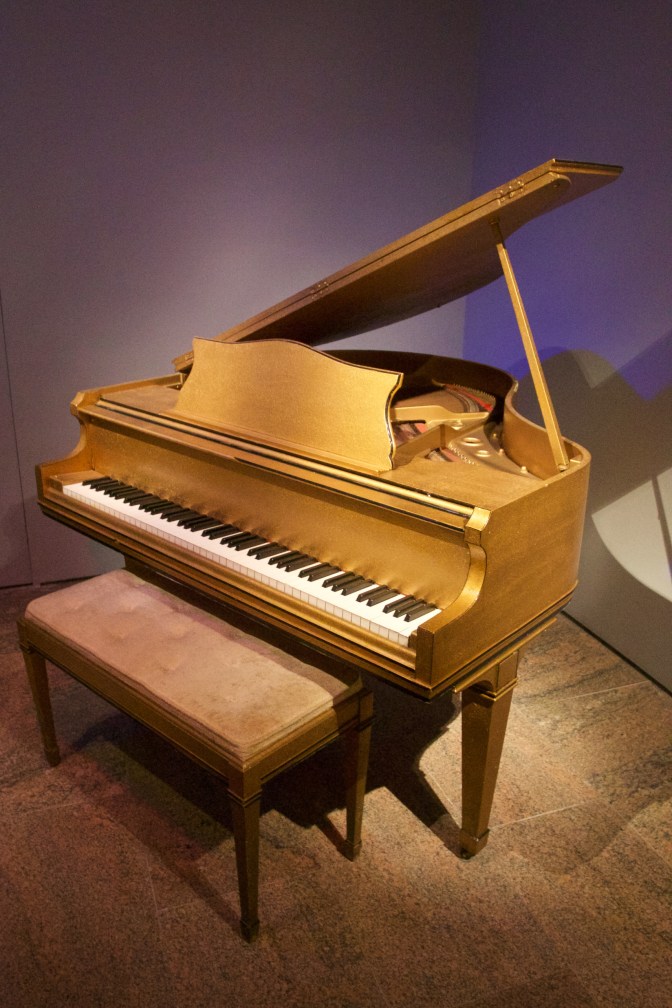 Wooden piano with top lifted. A bench is in front of the piano.