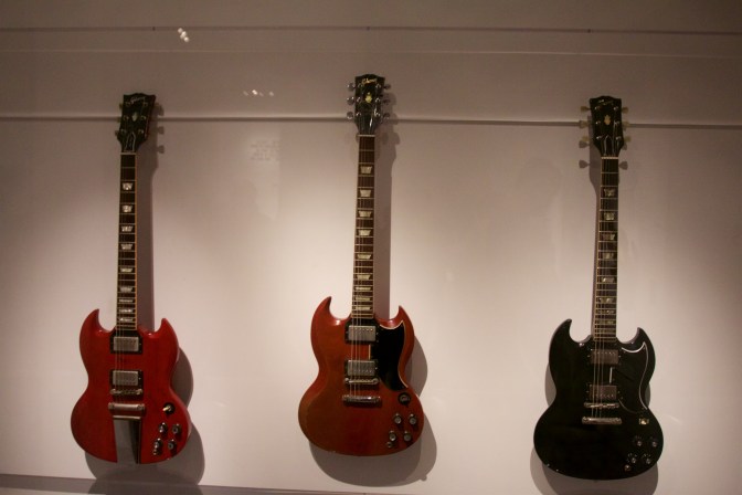 Three Gibson SG guitars - red one on left, red one in center, and black one on right.