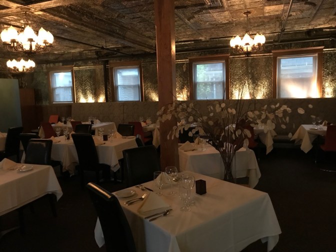 Interior of dining room of Tides Hotel. Tinwork is on ceiling and walls, and chandeliers hang from the ceiling.