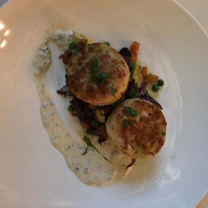 Two crab cakes on a bed of potatoes and vegetables.