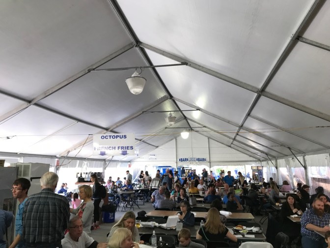 Tent with people dining. Signs point to different food stations.