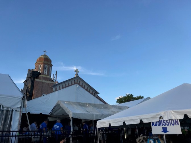 White tents in front of Greek Orthodox church (spire visible in background).