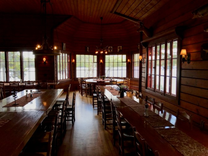 Dining room with long tables in foreground, and a series of windows offering a panoramic view of the outdoors.