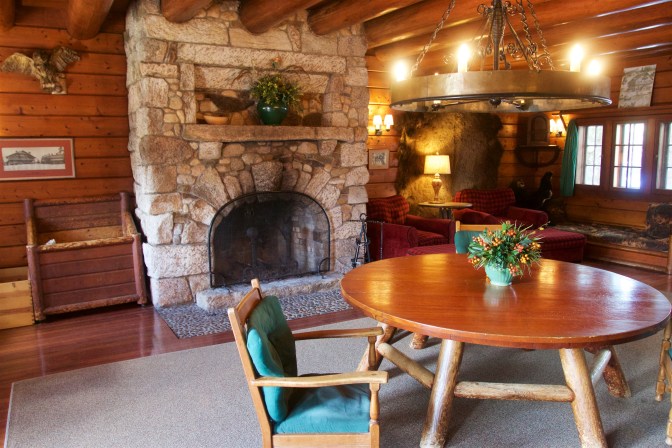 Lobby of Lodge, with chandelier, fireplace, and round wooden table with chairs.