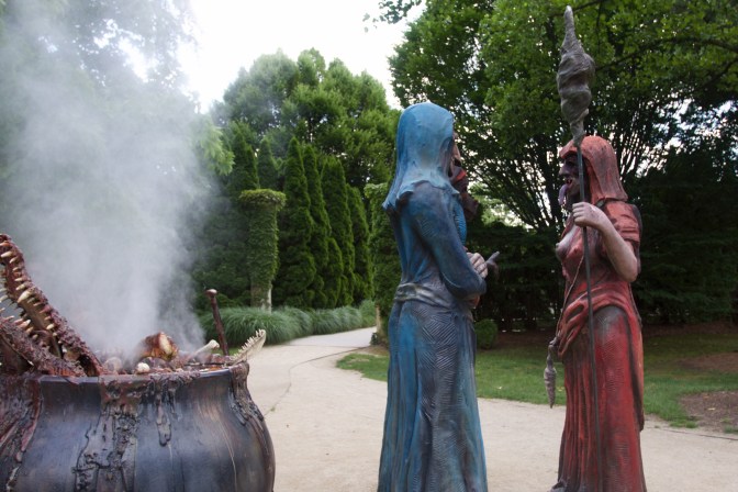Three witches standing beside a boiling cauldron.