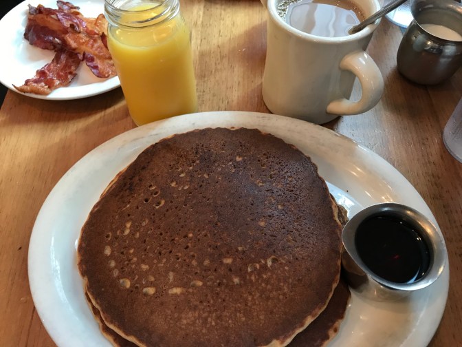 Photo of pancakes, orange juice, and coffee on table.