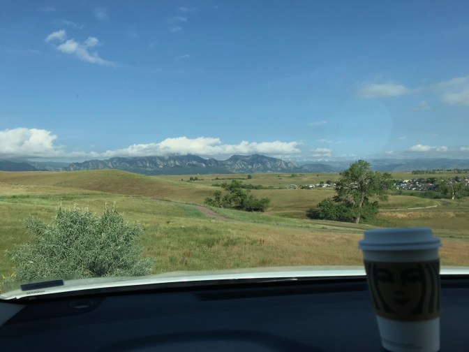 View of mountains through car windshield, with cup of coffee in foreground on dashboard.
