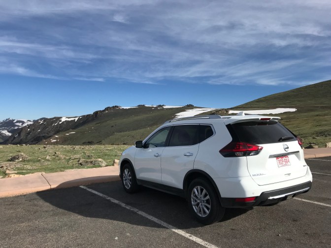 White Nissan Rogue SUV parked in front of mountains.