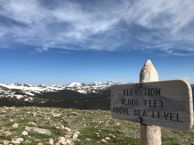 Wooden sign that says ELEVATION 12,005 FEET ABOVE SES LEVEL, with mountains in background.