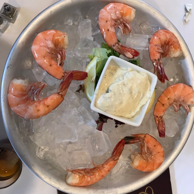 Metal bowl with chilled shrimp on ice, with aioli sauce in white bowl in middle of dish.