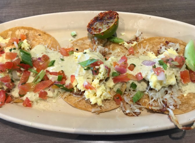 Three breakfast tacos with eggs, cheese, salsa, and hollandaise sauce.