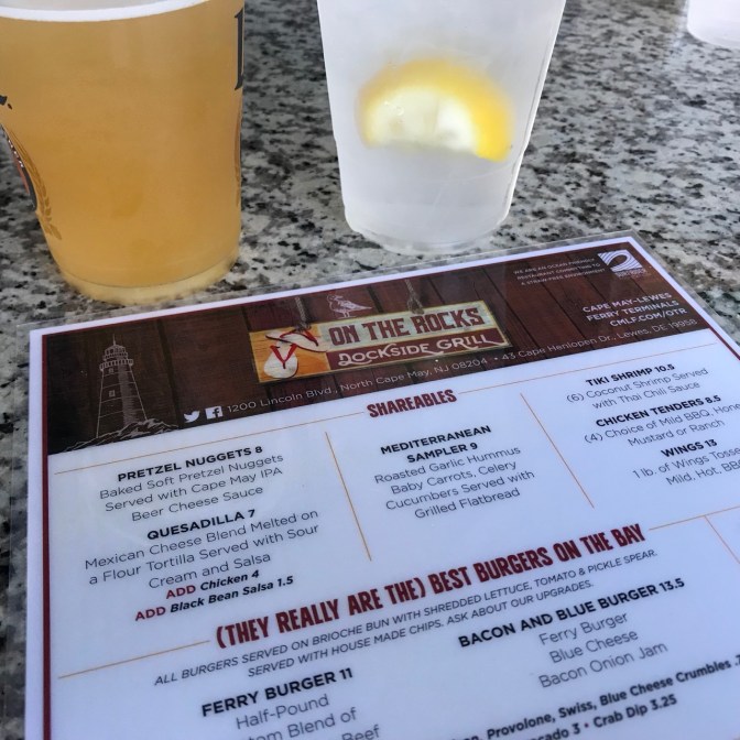 Menu of On the Rocks Dockside Grill, with a beer and a mixed drink in the background.