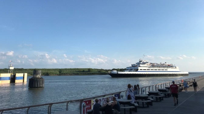 Cape May - Lewes Ferry arriving at Cape May Ferry terminal, with people at tables along pier in foreground.