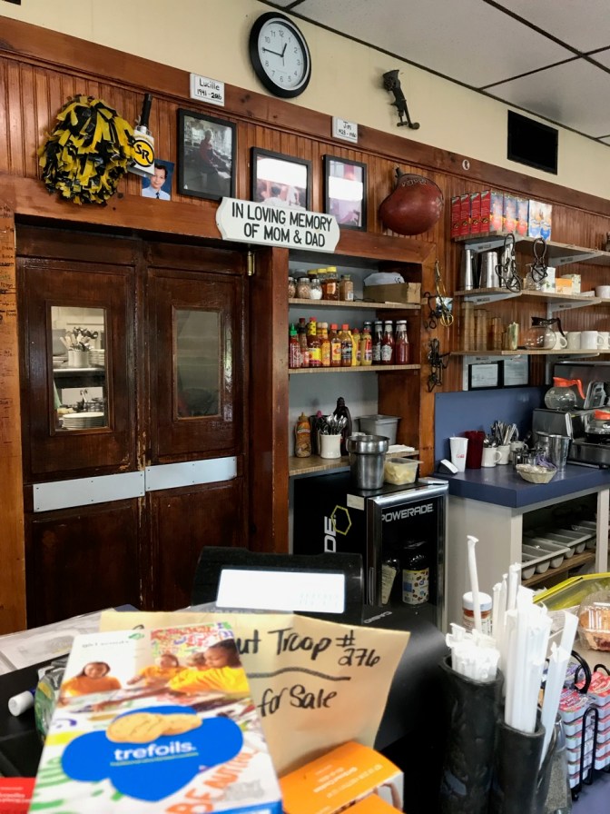 Area behind counter, with pictures of Lucille and her husband above kitchen door and a sign that says IN LOVING MEMORY OF MOM AND DAD.