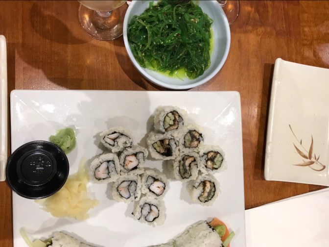 Sushi on square white plate, with seaweed salad in white bowl beside it.
