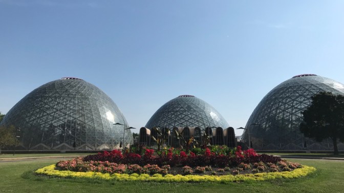 Three of the domes of Mitchell Park Conservatory with flowers and plants in the foreground.
