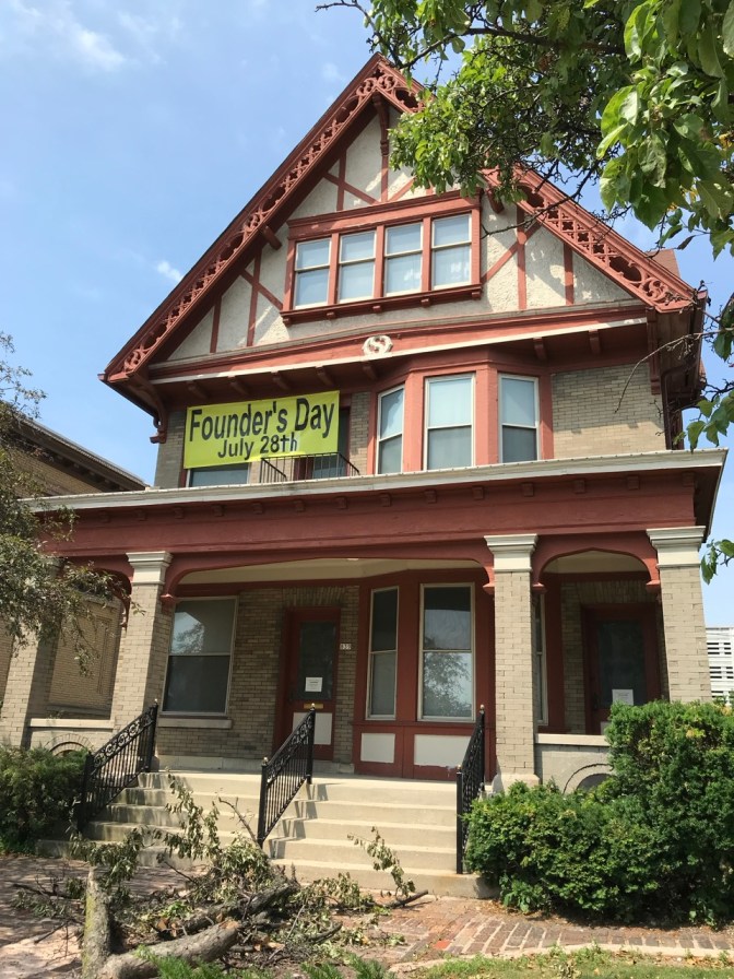 Exterior of Chudnow Museum of Yesteryear with a sign that says FOUNDER'S DAY JULY 28TH hanging from second floor window.