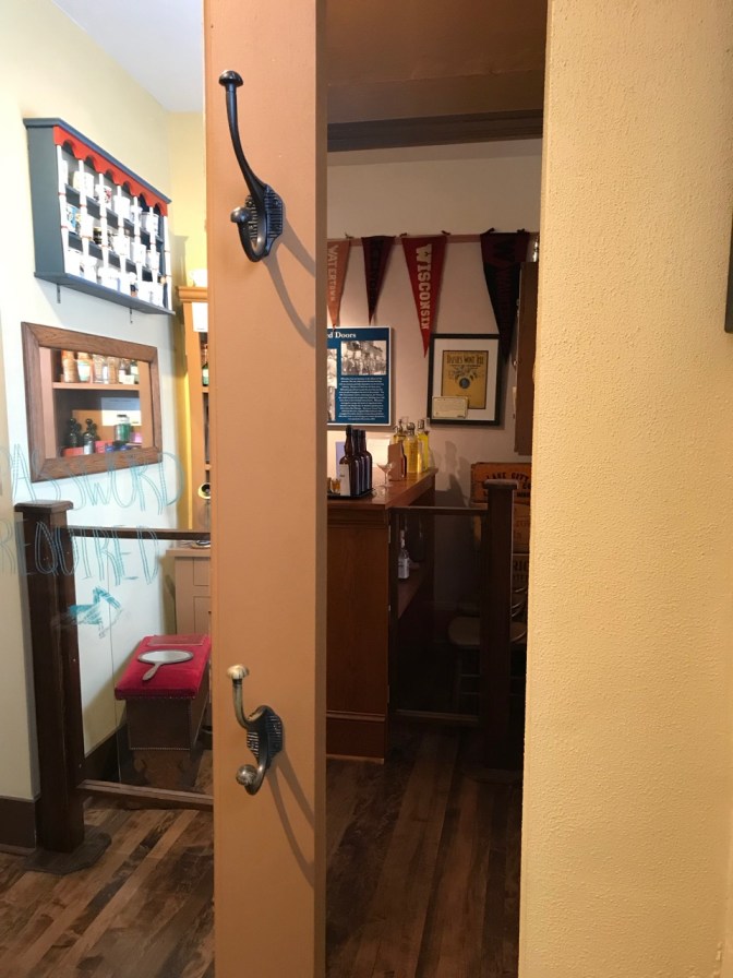 Mirror door pulled to the side, with a speakeasy in view in the next room.