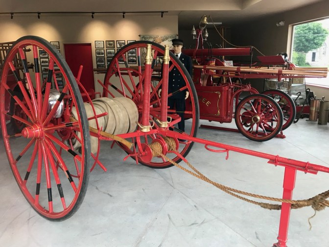 Red cart carrying a hose and an old horse-drawn fire engine.