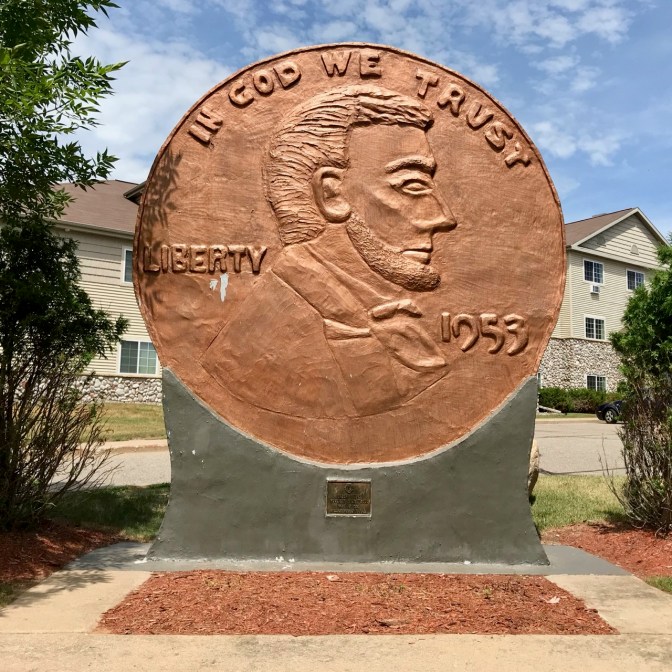 World's Largest Penny, on stand, with building in background. Penny says IN GOD WE TRUST LIBERTY 1953.