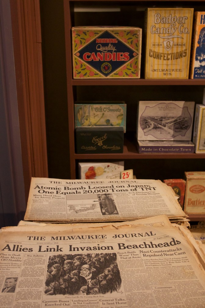 Newsstand with WWII-era newspapers that have headlines for atomic bomb dropped on Japan and allied invasion of France.