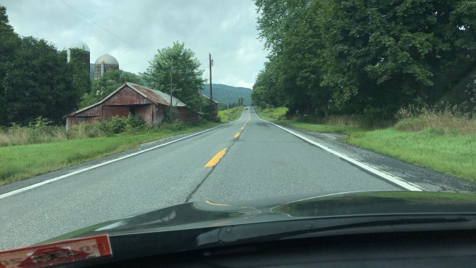Two-lane road with abandoned barn and silos on left.