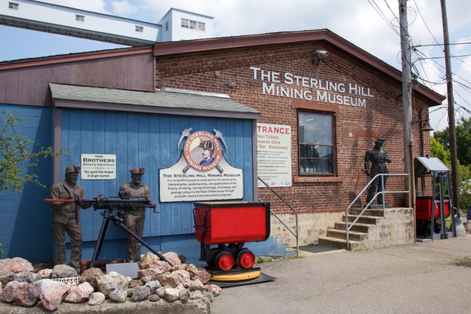 Exterior of visitor center, with statues of miners, a mining cart, and lettering on building that says THE STERLING HILL MINING MUSEUM.