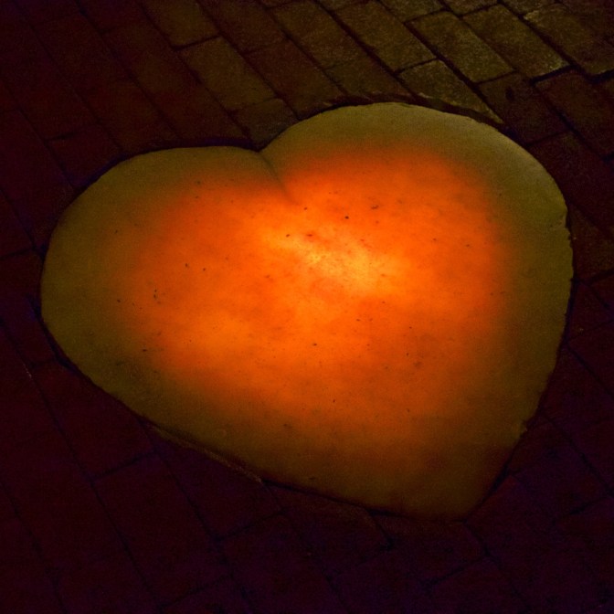 Heart made of calcite, lit from behind, on brick floor.