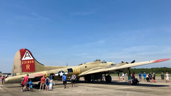 B-17 Flying Fortress bomber parked on tarmac, with people walking around it.