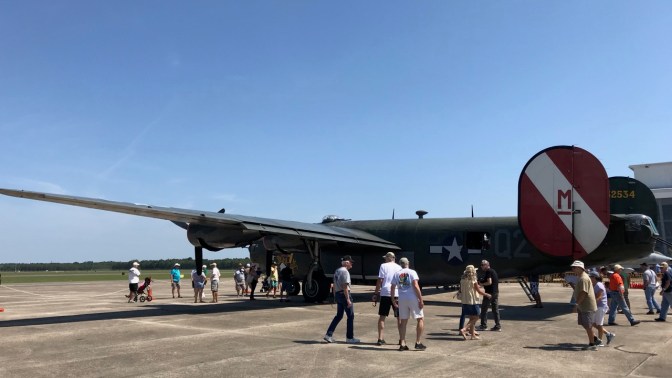 B-24 Liberator parked on tarmac with people milling around it.
