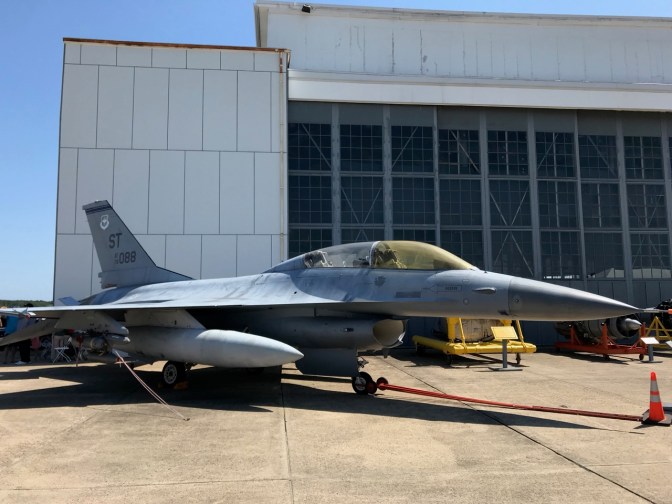 F-16 Falcon parked outside, beside hangar.
