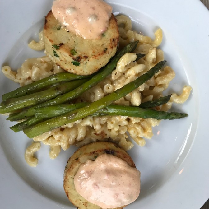 White plate with two crab cakes, macaroni and cheese, and grilled asparagus.